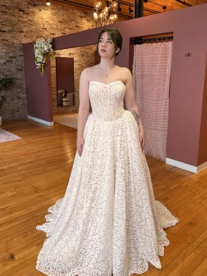 Bride in strapless lace wedding gown in boutique with brick walls and pink partitions.
